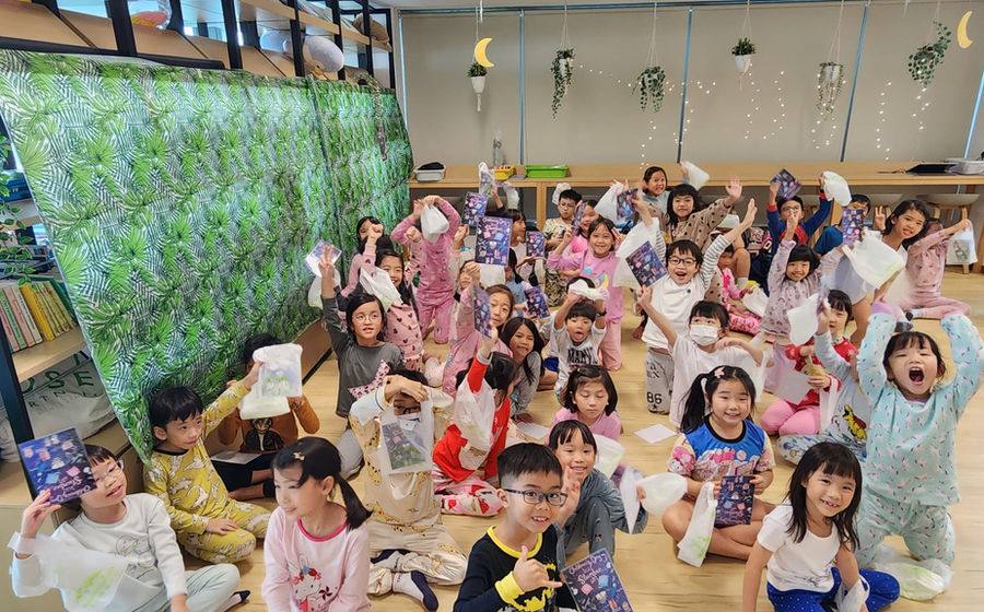 A large group of children in pyjamas cheering at a Kids & Co pyjama party.