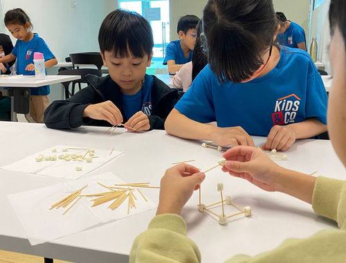 Close-up of children constructing a spaghetti tower.